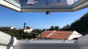 A view from a window with a security camera, overlooking a residential area with red-tiled roofs and white buildings. - A house in Caloura - Blue & Beach (Caloura)