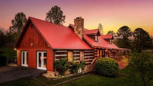 Uma cabana de toras com telhado de metal vermelho, chaminé de pedra e varanda com área de estar externa.
