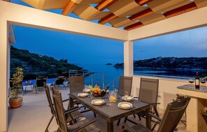 An outdoor dining area with a table set for two, overlooking a body of water and a hilly landscape. - Beach front home in Vela Luka (Vela Luka)