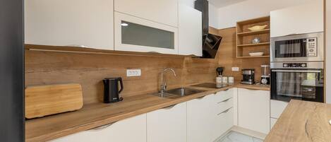 A modern kitchen with white cabinets, a wooden countertop, a coffee maker, a kettle, and a built-in oven.