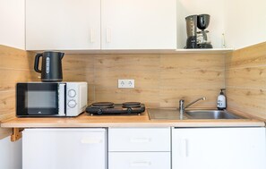 Una cuina compacta amb microones, torradora, bullidor, cafetera i un rentaplat.