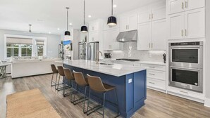 A modern kitchen with white cabinets, a blue island, stainless steel appliances, and pendant lighting. - Luxury Beach House: Rooftop Jacuzzi & Family Fun (Inlet Beach)