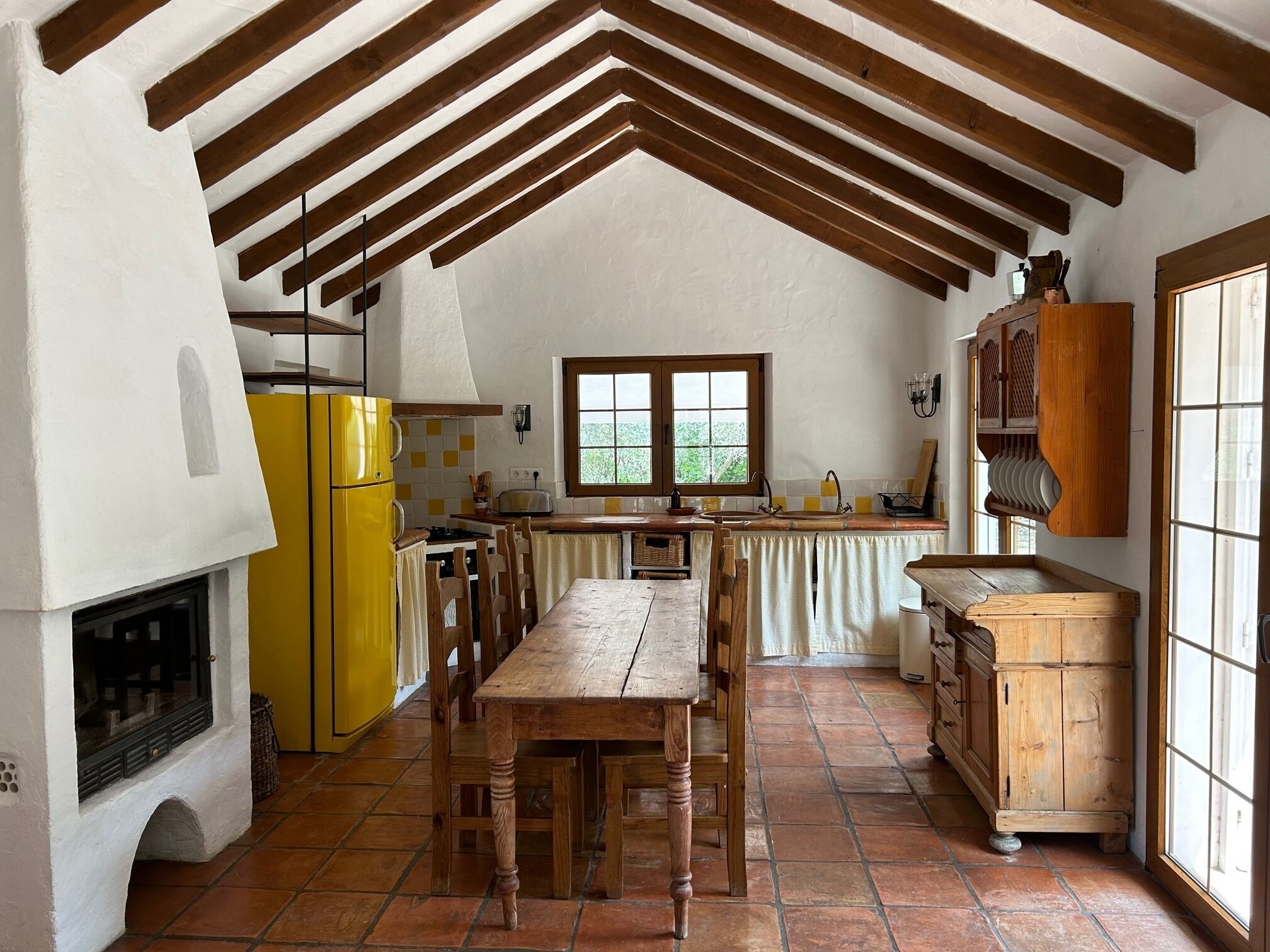 A rustic kitchen with a wooden table, chairs, a yellow refrigerator, and a wooden cabinet.