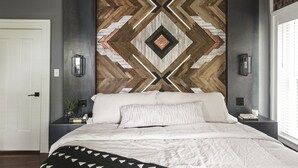Una camera da letto con un letto grande, una parete decorata con motivi geometrici e un comodino con una lampada.