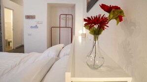 A hotel room with a bed, a bedside table with a vase of flowers, a wardrobe, and a door leading to another room. - APT. - Studio apartment in the historic center of Naples (Napoli)