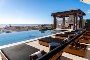 An infinity pool with lounge chairs, a pergola, and a view of the ocean.