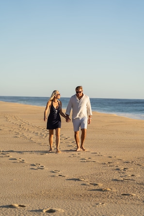 A couple walking hand in hand on a sandy beach with the ocean in the background.