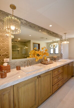 A modern bathroom with a large mirror, two sinks, wooden cabinets, and decorative lighting.