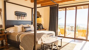 Un dormitorio con una cama grande, una mesita de noche, una lámpara y vistas al océano a través de puertas correderas de cristal.