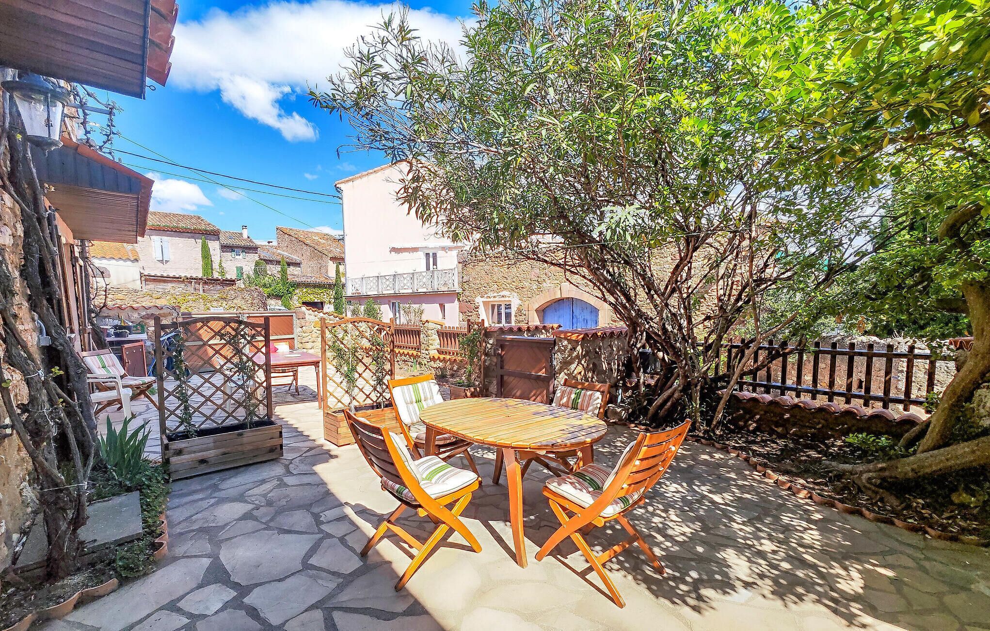 A patio with a round table and four chairs, surrounded by stone flooring and plants.