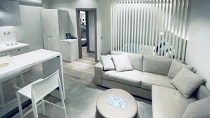 A modern living room with a sofa, a dining table with chairs, a small kitchenette, and a bathroom visible through an open door. - Appartamento - Angolo di Rio (Riomaggiore)