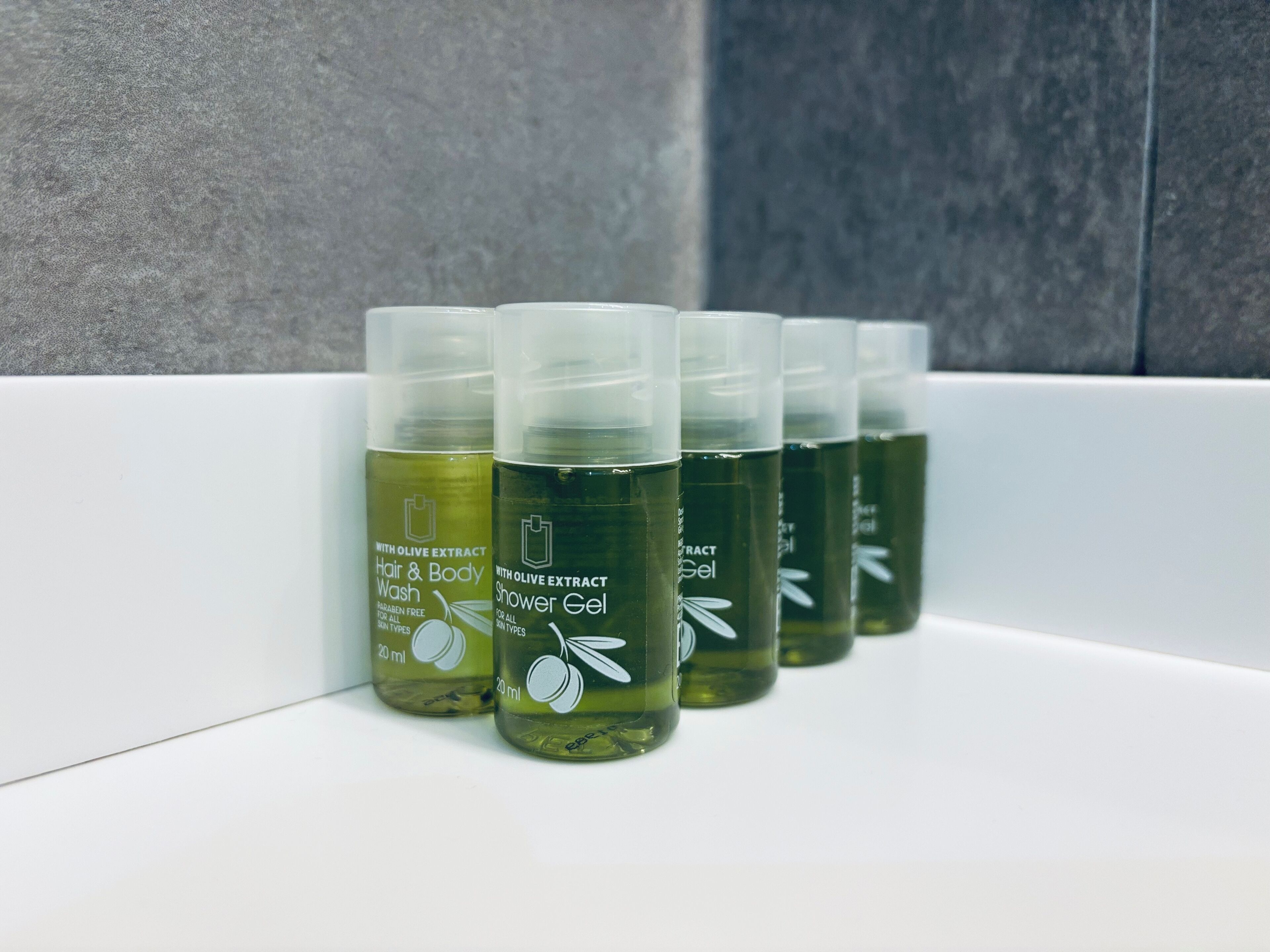 A row of olive oil-based hair and body wash bottles in a bathroom setting.