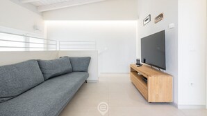 A modern living room with a grey sofa, a wooden TV stand, and a large flat-screen TV. - Villetta Ada: a little corner of paradise just steps from Poetto (Cagliari)