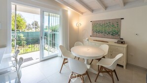 A modern dining area with a round table and white chairs, a sliding glass door leading to a balcony, and a large abstract painting on the wall. - Villetta Ada: a little corner of paradise just steps from Poetto (Cagliari)