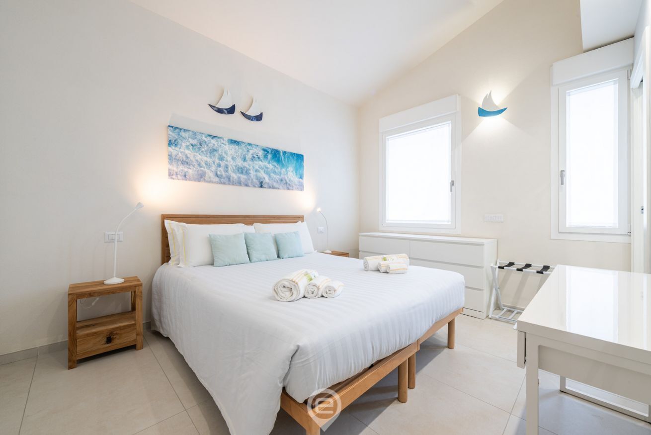 A bedroom with a bed, bedside tables, a painting, and a window.