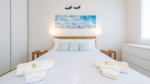 A neatly made bed with white linens and striped towels, a wooden headboard, and a framed picture of waves on the wall. - Villetta Ada: a little corner of paradise just steps from Poetto (Cagliari)