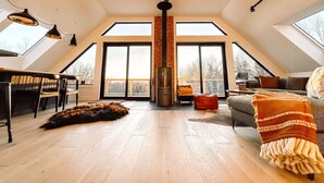 Un loft spacieux avec de hauts plafonds, un ventilateur de plafond central, de grandes fenêtres et un coin salon confortable avec un canapé et un tapis.