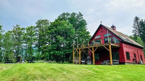 Une maison en bois rouge, dotée d’un balcon, entourée d’arbres et bordée d’une pelouse verdoyante.