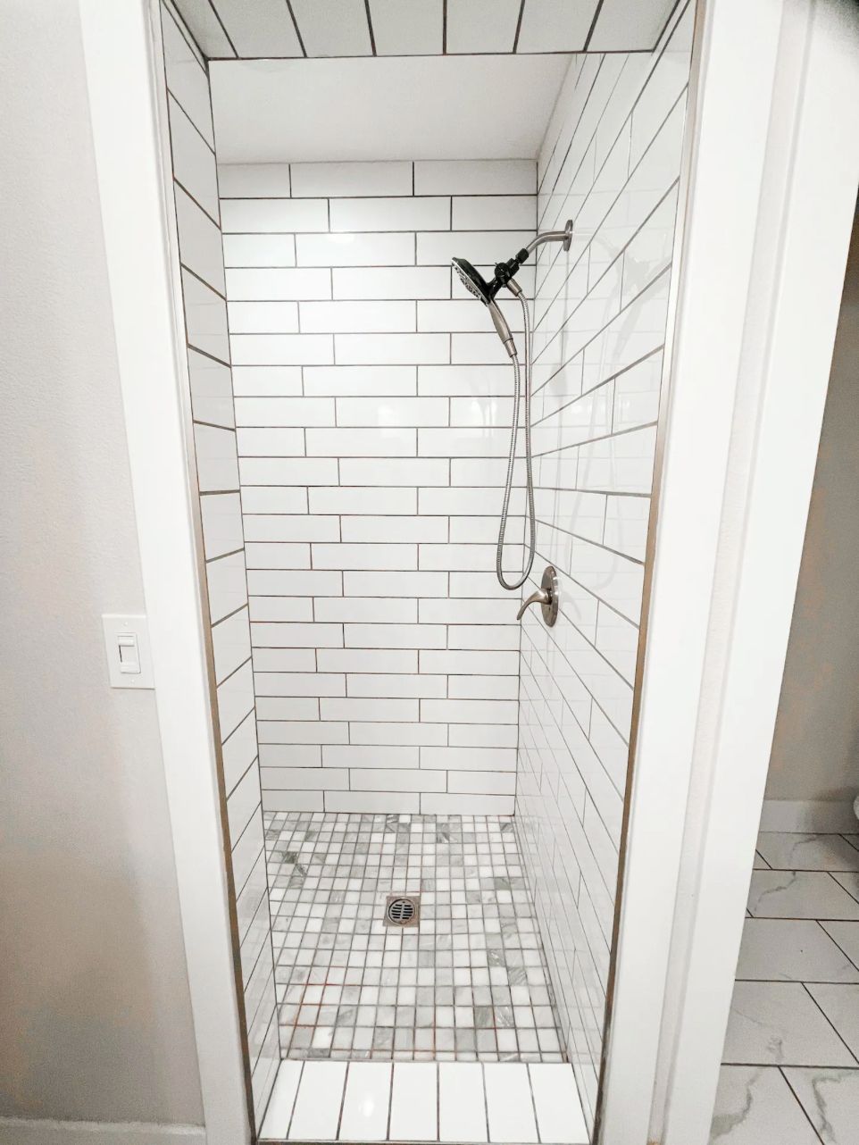 Une petite douche carrelée, dotée d’un pommeau de douche à main et d’un robinet fixé au mur.