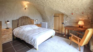 Quarto com cabeceira de madeira, cama com roupa de cama branca, escrivaninha com cadeira e radiador.