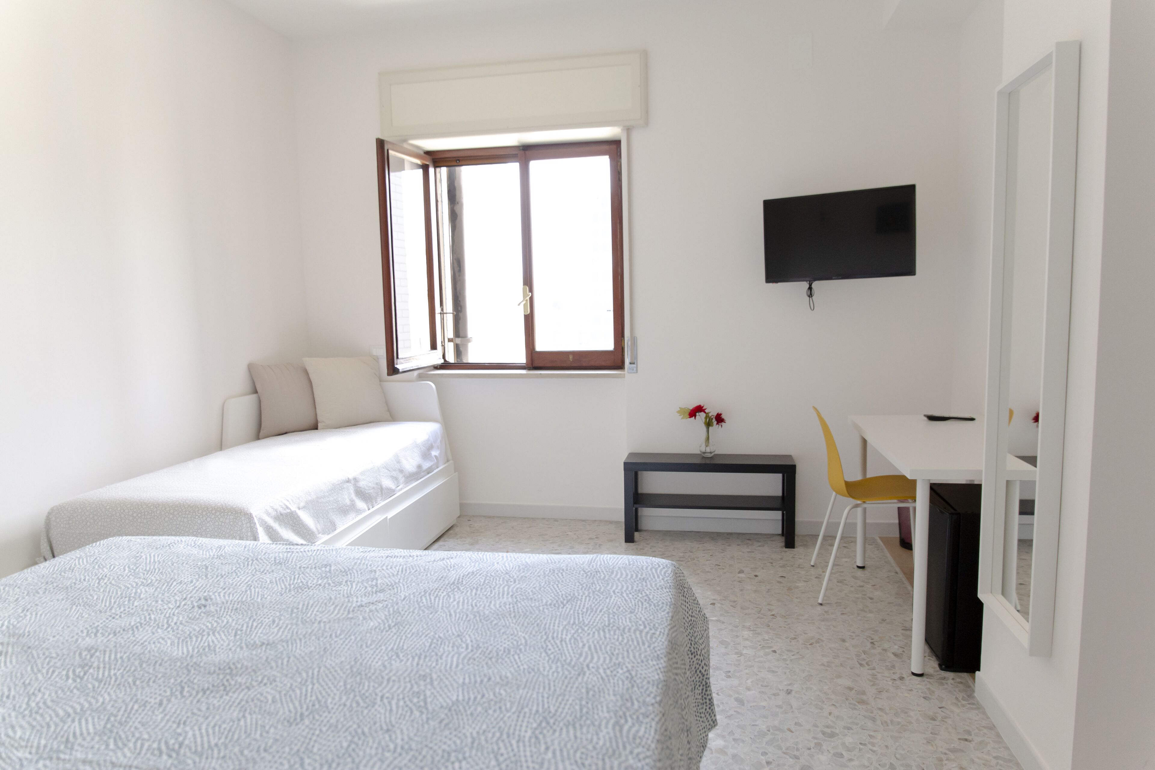 A bedroom with two beds, a desk, a chair, a TV, and a window.