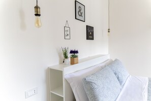 A bedroom with a white bed, a bedside table with a vase of flowers, and wall-mounted light fixtures. - Superior King Room (Napoli)