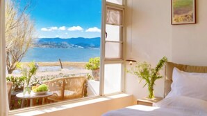 Ein Schlafzimmer mit großem Fenster, einem Bett, einem Nachttisch und Blick auf ein Gewässer und Berge.