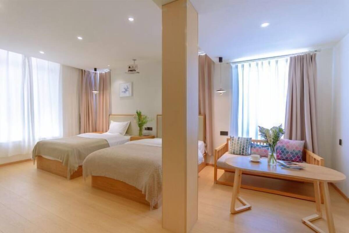A hotel room with two beds, a wooden table, and a view of the outdoors.