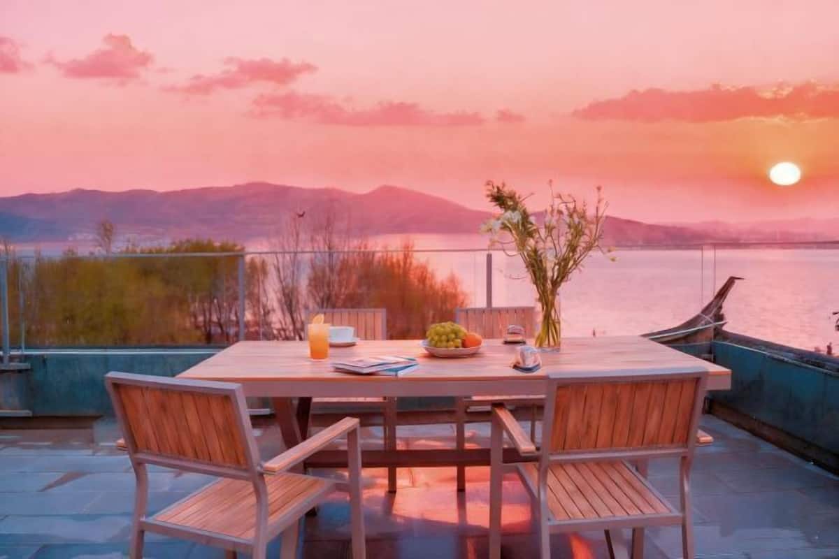 A table set outdoors with chairs, a vase with flowers, a bowl of fruit, and a drink.
