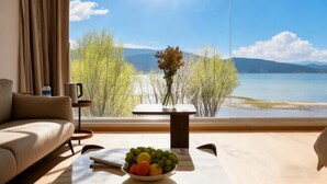 Ein modernes Zimmer mit großem Fenster, einer Couch, einem kleinen Tisch mit Obstschale und einer Vase mit Blumen.
