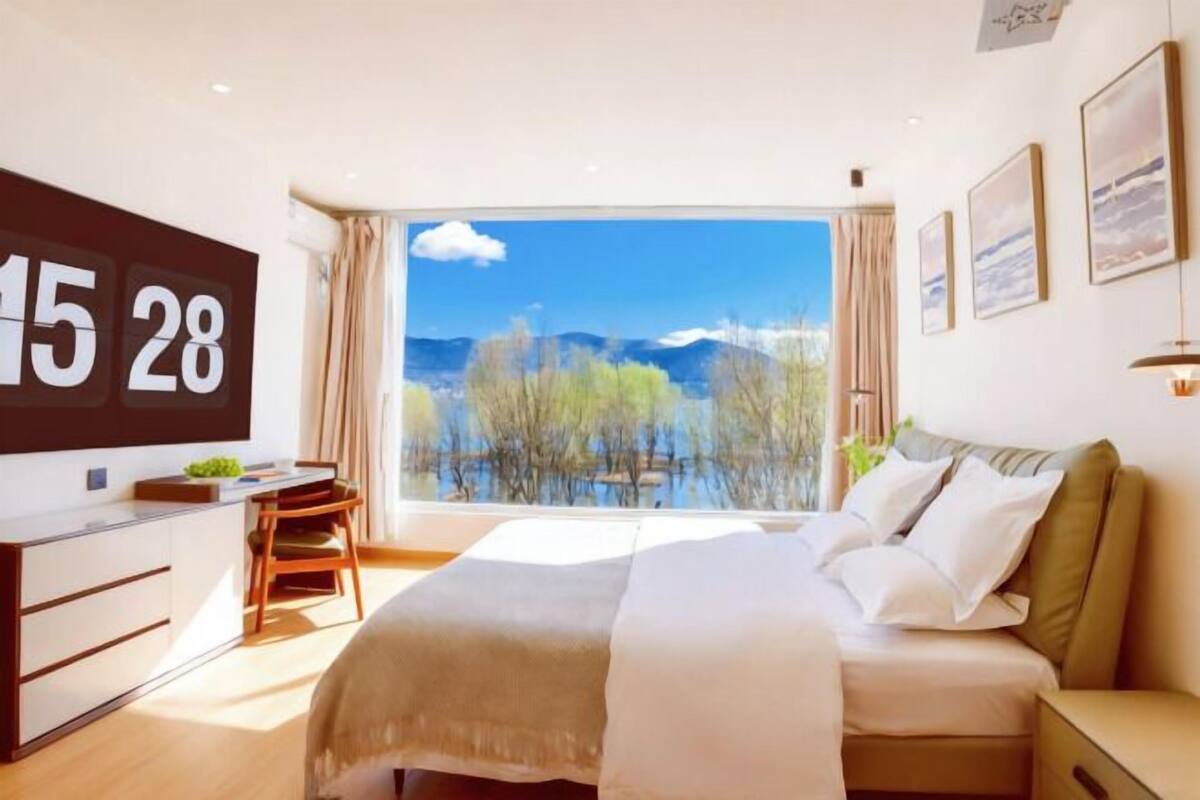 A hotel room with a large window, a bed, a desk, and a chair.
