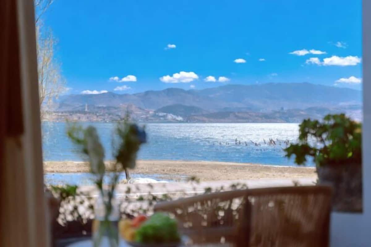 A view from a window overlooking a beach with mountains in the distance.