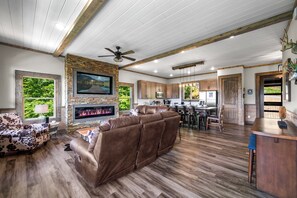 A spacious living area with a fireplace, a large brown sectional sofa, and a dining area with wooden flooring. - HUGE VIEW | Pool | Pool Table | Theater Room (Gatlinburg)