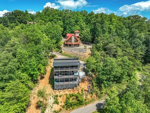 A modern building with a glass facade, situated on a hillside surrounded by dense forest. - HUGE VIEW | Pool | Pool Table | Theater Room (Gatlinburg)