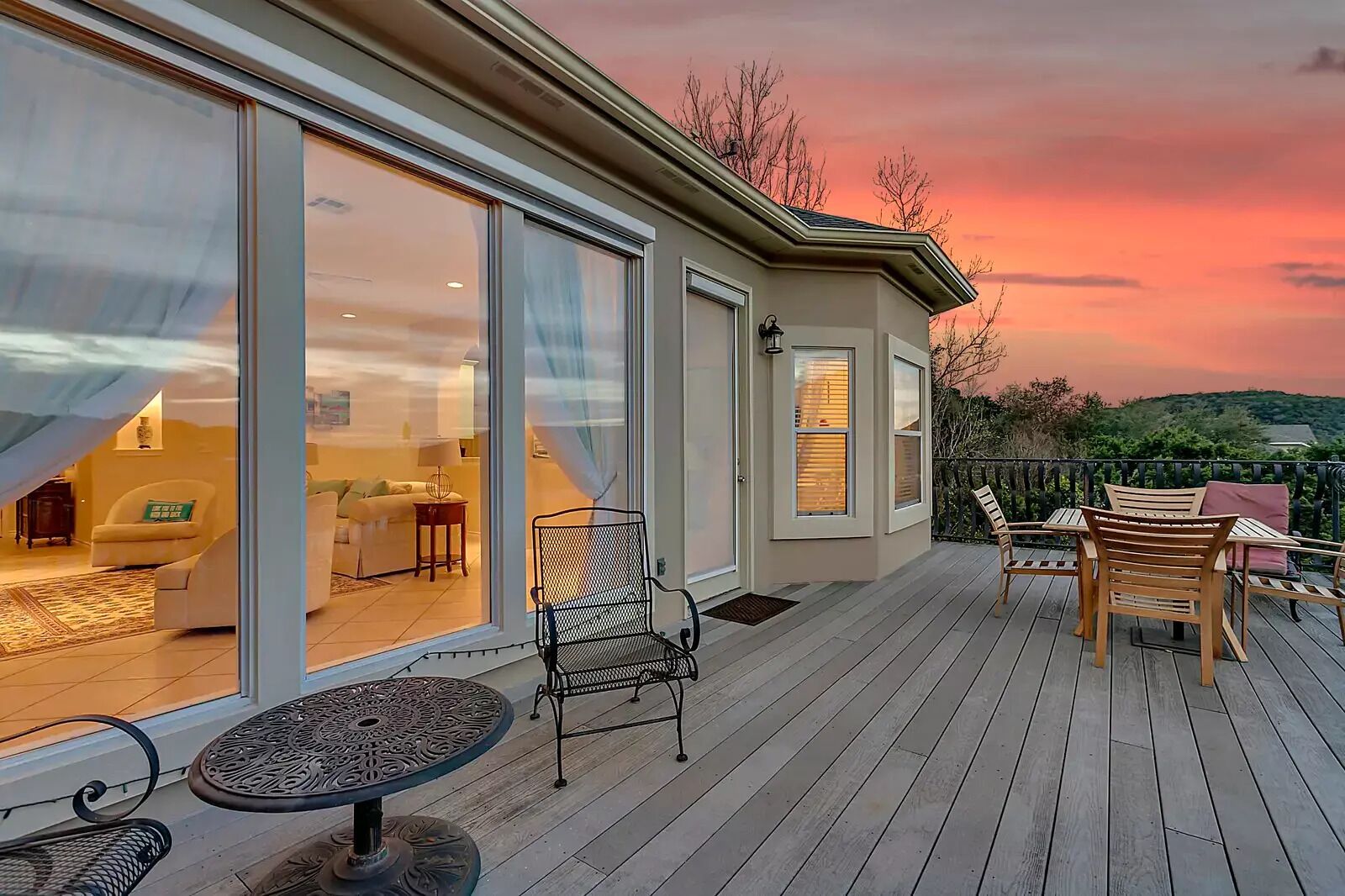 A modern house with a deck, large sliding glass doors leading to a living room, and a scenic sunset view.
