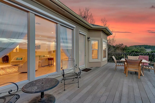 Una casa moderna con terraza, grandes puertas correderas de vidrio que dan a una sala de estar y una vista panorámica del atardecer.