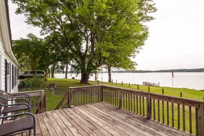 Eine Holzterrasse mit Geländer, die auf einen See blickt, mit einer Rasenfläche und einem geparkten Fahrzeug in der Nähe.