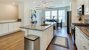A modern kitchen with white cabinets, a granite countertop, a stainless steel range hood, and a dining area with a table and chairs.