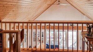 A high-ceilinged room with wooden beams, a ceiling fan, and a view of an outdoor deck through a window with a wooden railing. - Gorgeous home in Ljung with kitchen (Ljung)