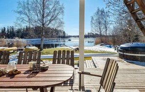 A wooden deck with a table and chairs, overlooking a lake with a dock and a boat. - Gorgeous home in Ljung with kitchen (Ljung)