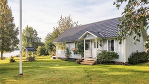 A two-story house with a porch, surrounded by a well-maintained lawn and trees. - Gorgeous home in Ljung with kitchen (Ljung)
