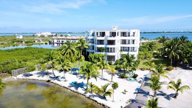 Un hotel de varios pisos con fachada blanca, situado en la playa, con palmeras y una playa de arena.