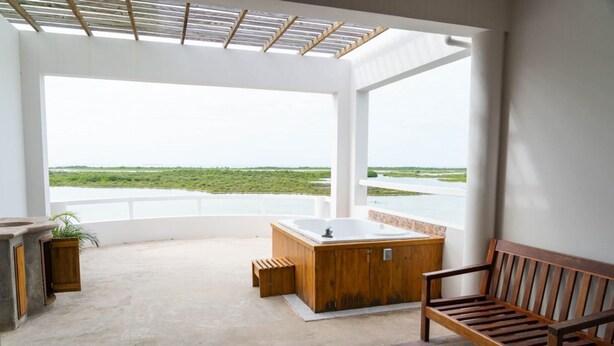 Un balcón amplio con una bañera de madera, un banco y vista a un cuerpo de agua.
