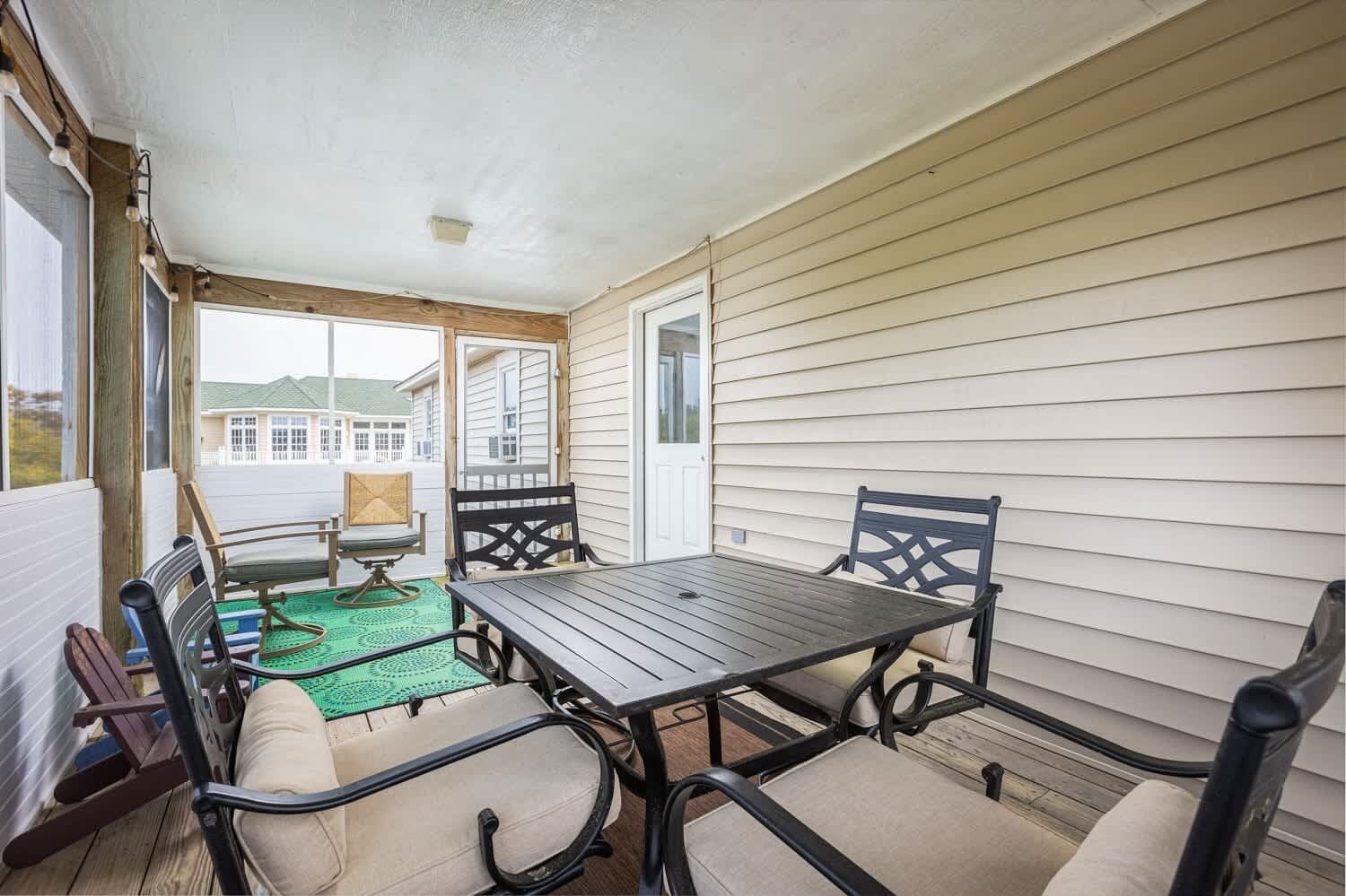 A covered patio with a table and chairs, a rocking chair, and a view of a house in the background.