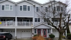 A multi-story residential building with a garage, a balcony, and a front door with a stone accent.