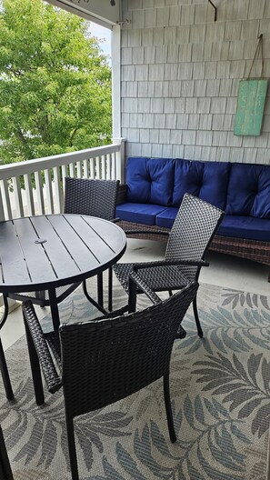 Un patio couvert avec une table ronde et deux fauteuils en osier, un canapé bleu et un mur décoratif.