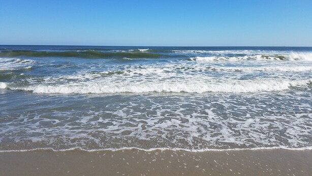 A beach with waves approaching the shore under a clear sky.
