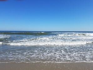 Une plage où les vagues se brisent près du rivage, sous un ciel dégagé.