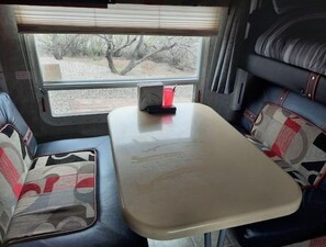 Relax in the spacious interior of this camper, featuring a central table and comfortable seating for two.