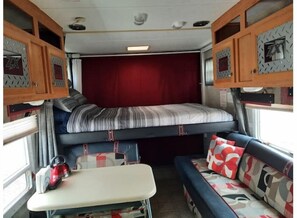 Compact RV interior with a central bed, cabinets, and a small table for refreshments.